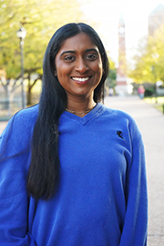 A headshot photo of Kirti Madhu with a clocktower and trees in the background.