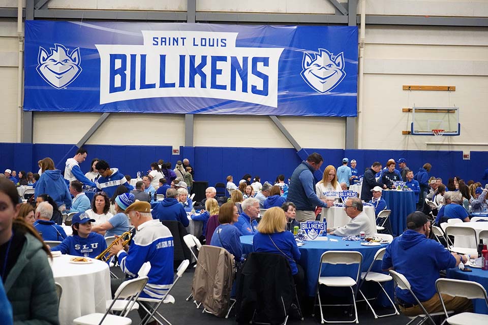 Billiken Fan Fest 2026 People sit at tables eating and talking. A large banner in the background says Saint Louis Billikens.