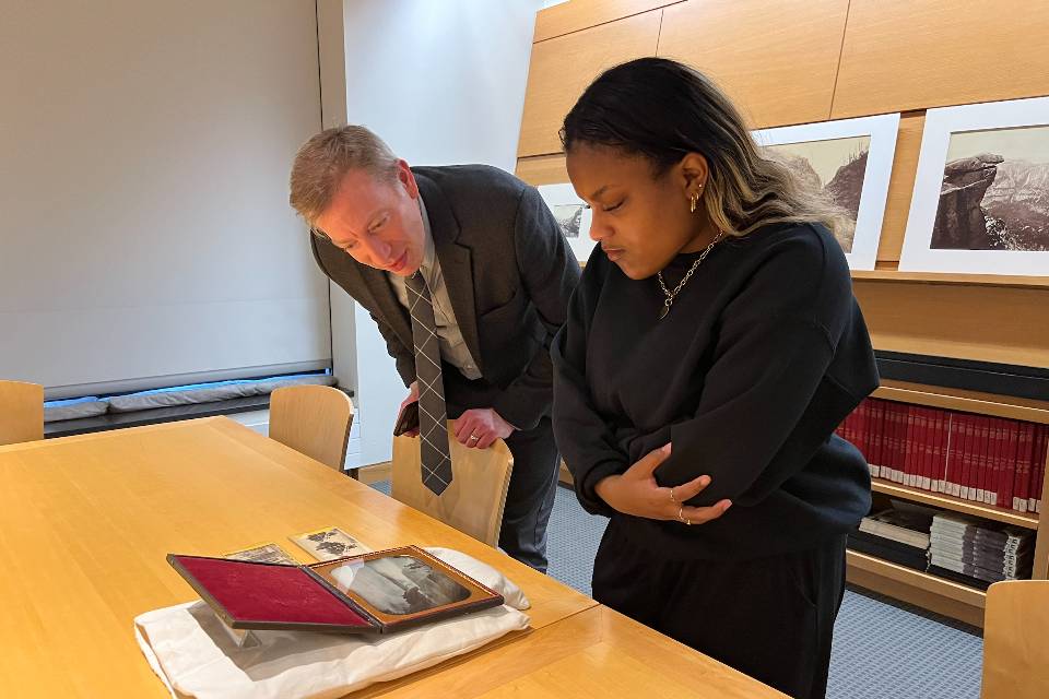 A student and professor bend over a table looking at a manuscript