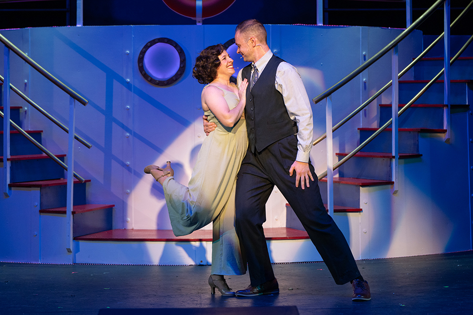 A man and a woman stand in a dance pose and smile