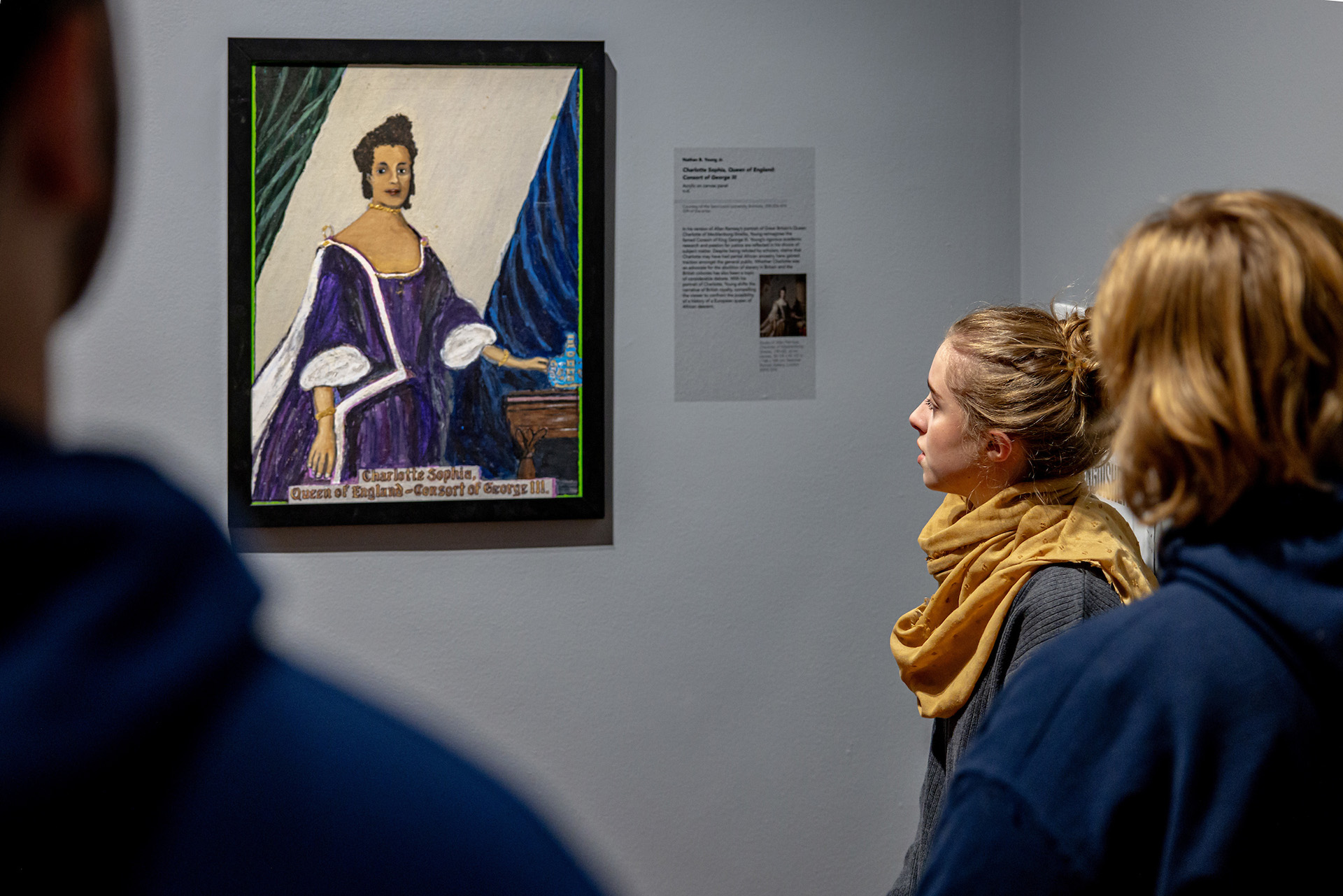 A blonde student in a yellow scarf studies a painting