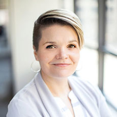 Katie Heiden Rootes, headshot. She is looking at the camera while wearing a grey sweater and light blouse.