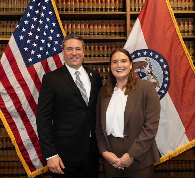 Paige Mitchell stands next to Missouri Attorney General Andrew Bailey between the Missouri State flag and the United States flag