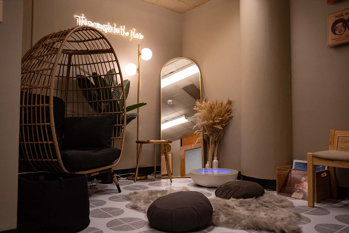 Image of a room with low lighting, a hanging chair with footrest, and cushions and a fluffy carpet on the floor.