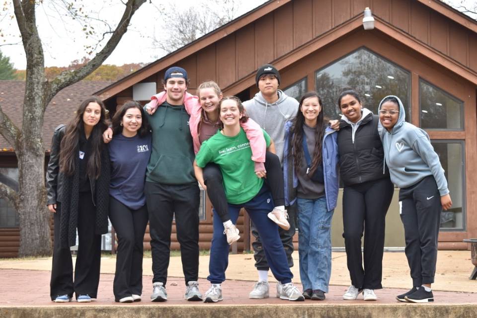 A group of students pose for a photo outside of a retreat center in the woods.