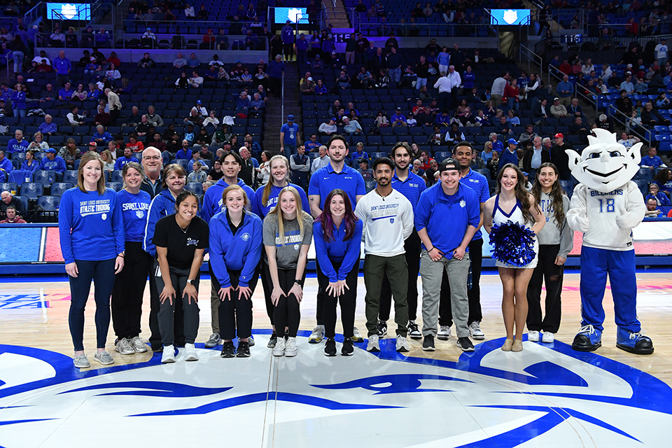 A group of people pose with SLU's Billiken on a basketball court.