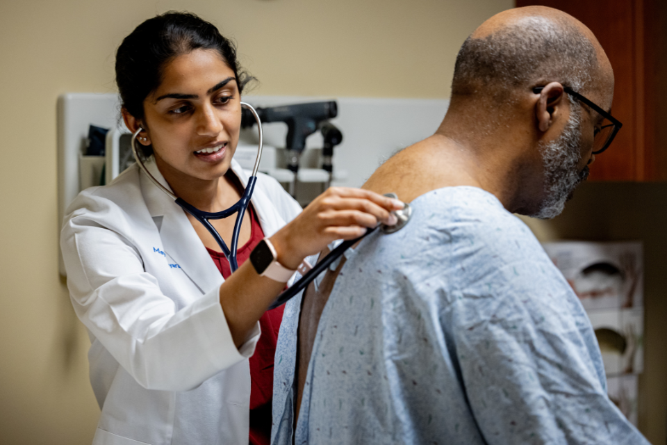 A nurse practitioner listens to lung sounds of an adult.