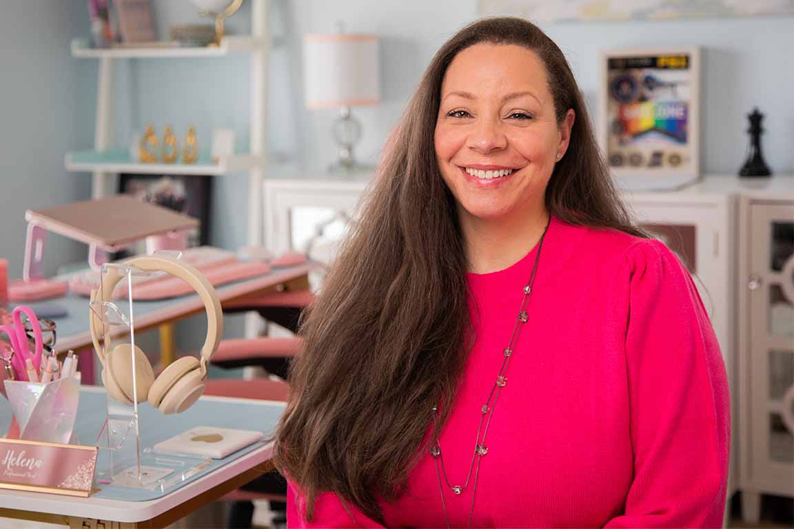 A woman in a pink shirt looking at the camera with a desk in the background