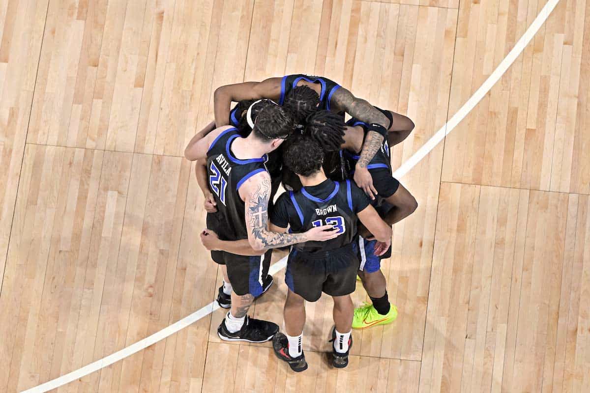 SLU Men's Basketball Members of the men's basketball team stand in a huddle in the middle of the court during a game.