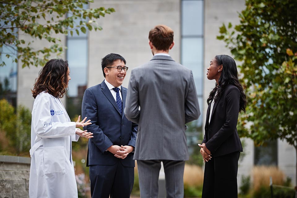 Four students in professional clothing stand and talk outside of SLU Hospital