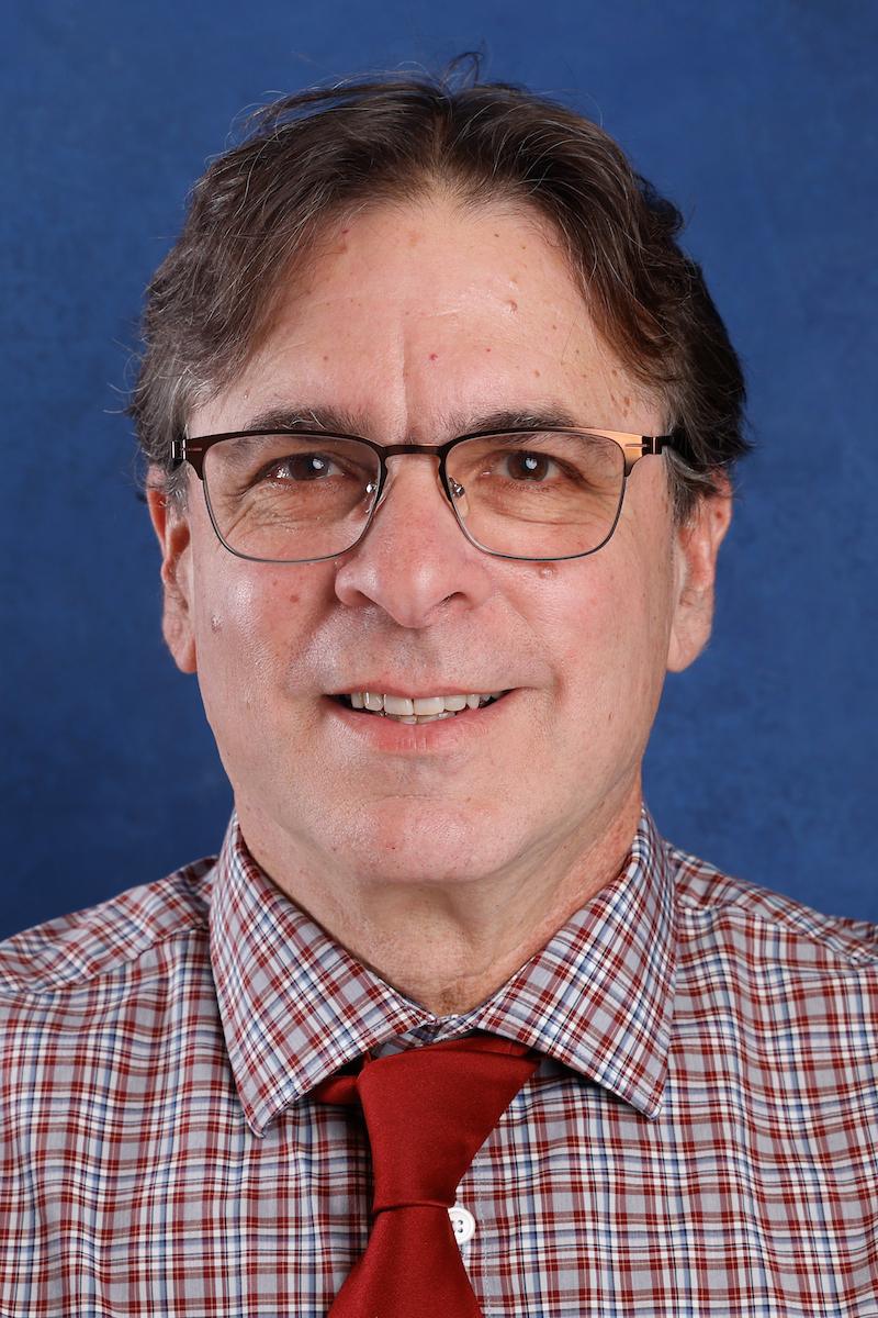 Dan Hanes, Ph.D., smiles in front of a blue background